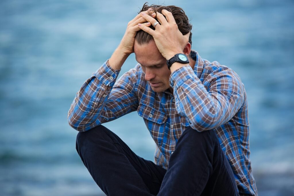 pexels photo 897817 897817 A man in a plaid shirt sits by the water looking distressed, symbolizing stress.